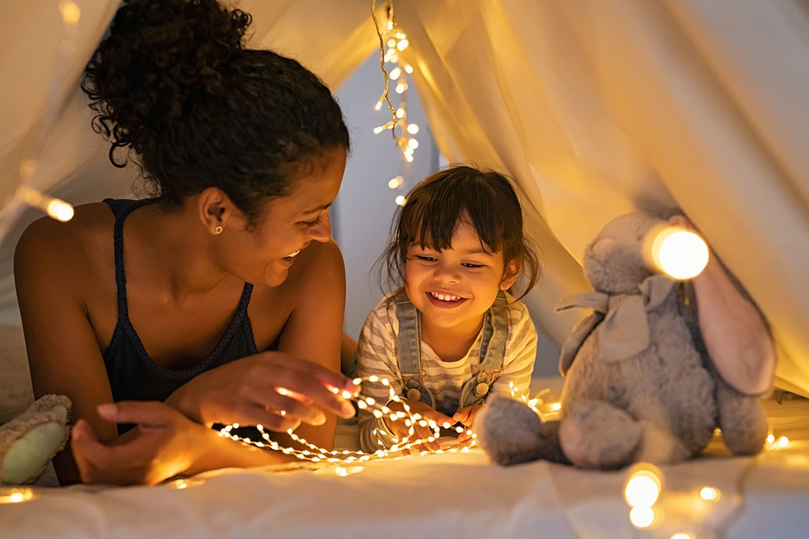 Mother and daughter lying in a blanket fort decorated with string lights