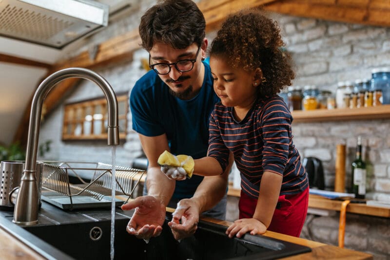 Parent and child washing hands at the kitchen sink next to an induction cooktop
